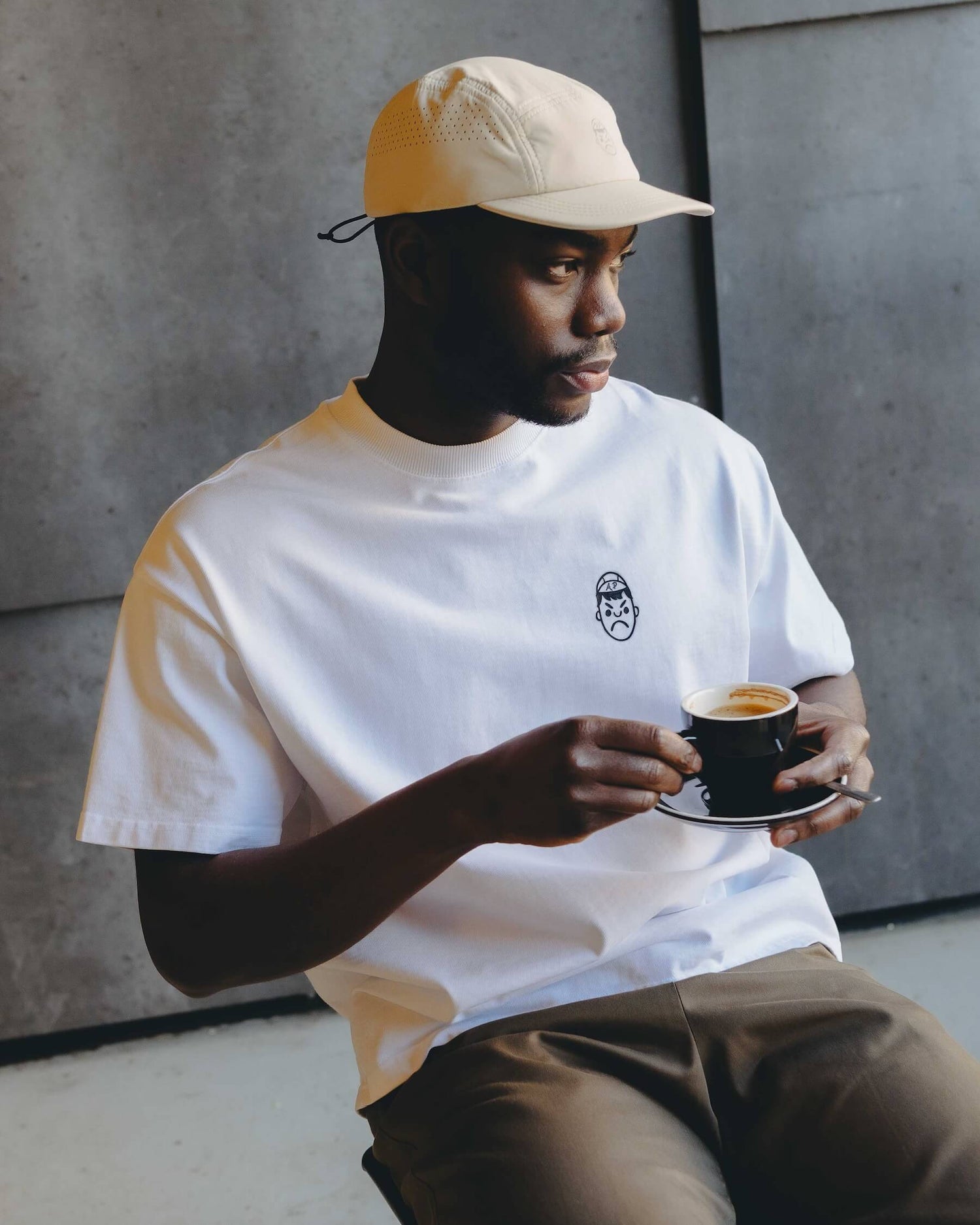 A man drinking a coffee wearing an Angry Pablo white oversized T-shirt