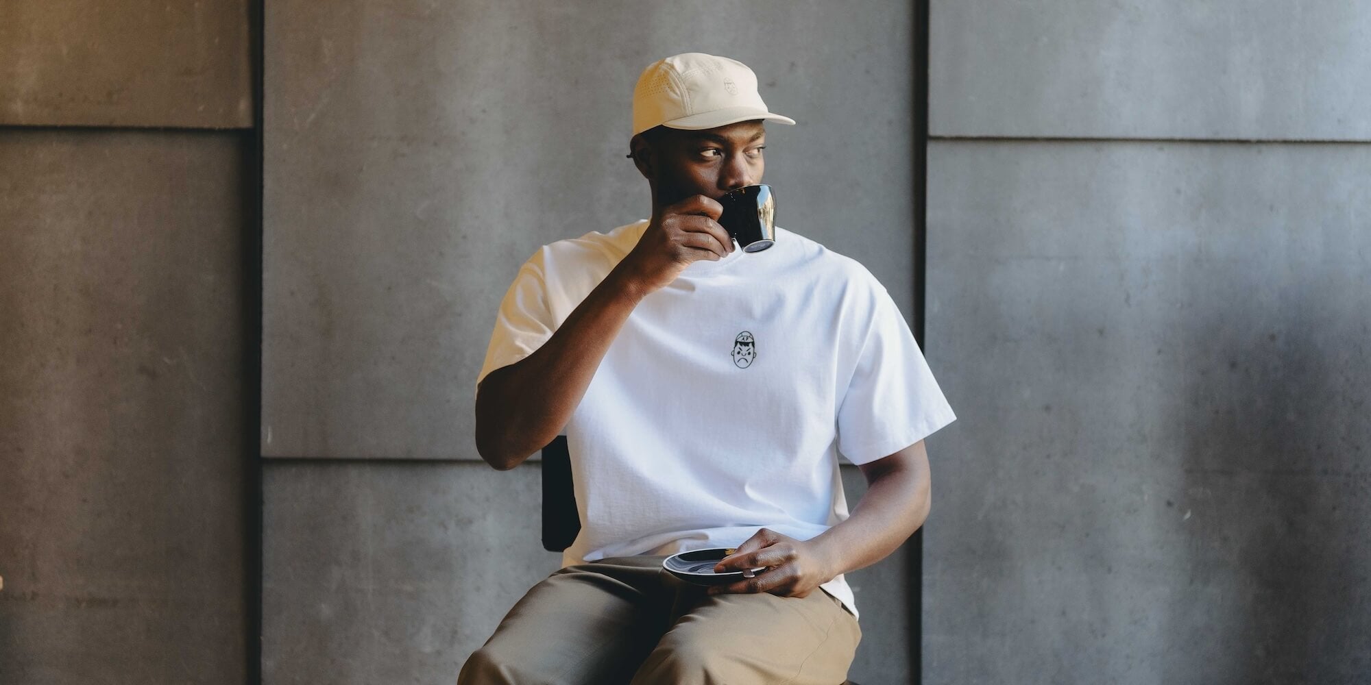 A man drinking a coffee whilst wearing an Angry Pablo Running Cap and a white oversized heavy tee