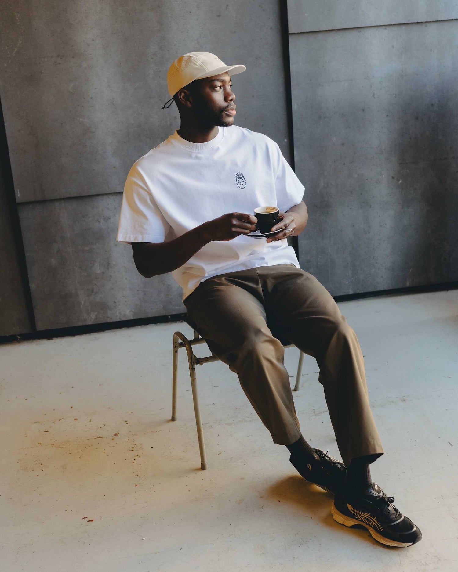 A man holding a coffee whilst wearing an Angry Pablo Running Cap and a white oversized heavy tee